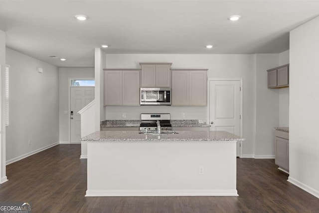 kitchen with light stone countertops, gray cabinets, stainless steel appliances, and an island with sink