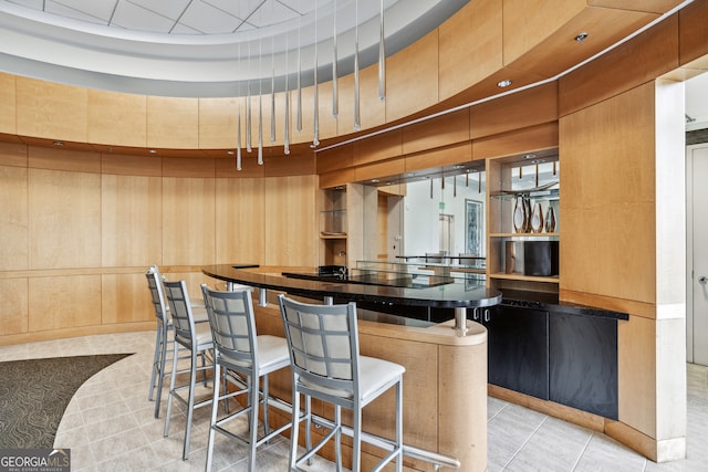 kitchen with a kitchen bar, wood walls, light tile patterned floors, and a high ceiling