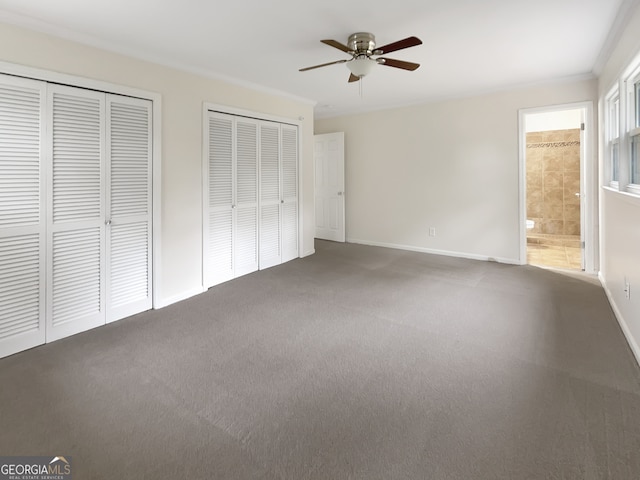 unfurnished bedroom featuring carpet flooring, two closets, ensuite bathroom, and ceiling fan