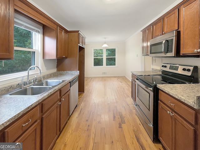 kitchen with light hardwood / wood-style flooring, stainless steel appliances, ornamental molding, sink, and pendant lighting