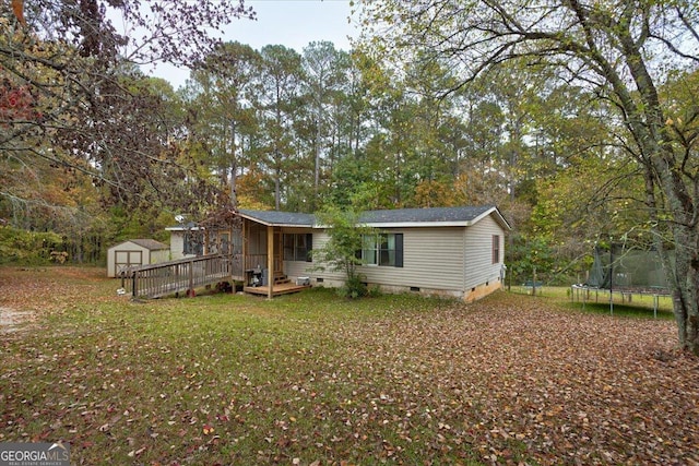 rear view of house with a deck, a yard, a trampoline, and a shed