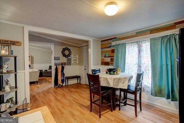 dining area with hardwood / wood-style flooring, ornamental molding, vaulted ceiling, and a textured ceiling