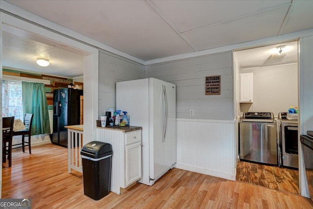 kitchen with washing machine and clothes dryer, white cabinetry, black refrigerator with ice dispenser, light wood-type flooring, and white refrigerator