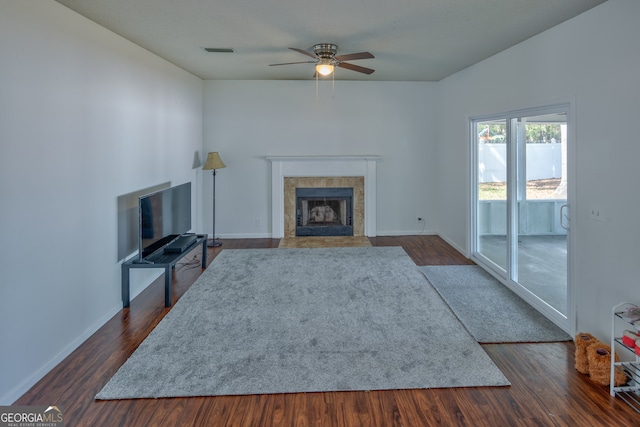 unfurnished living room featuring ceiling fan, a tiled fireplace, and dark hardwood / wood-style flooring