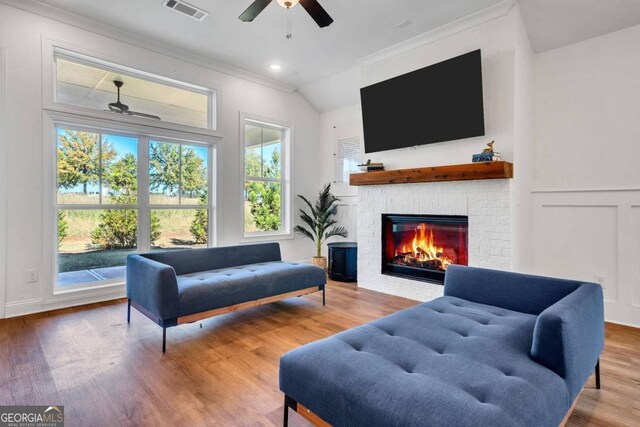 living room featuring a brick fireplace, hardwood / wood-style floors, ceiling fan, lofted ceiling, and ornamental molding