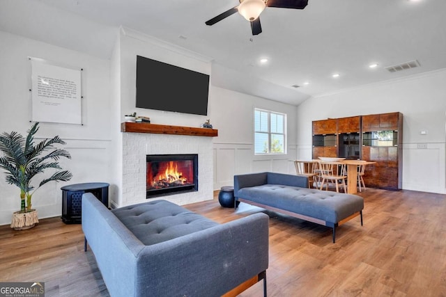 living room featuring crown molding, light hardwood / wood-style flooring, a fireplace, and ceiling fan