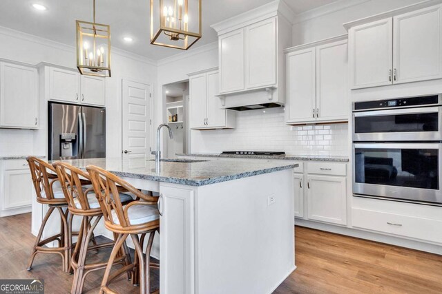 kitchen featuring a kitchen island with sink, stainless steel appliances, sink, pendant lighting, and white cabinets