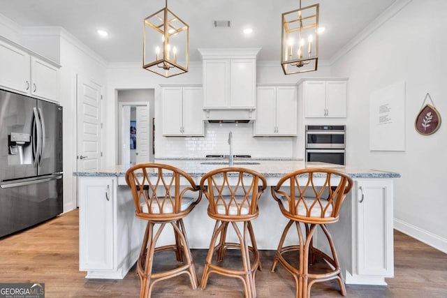 kitchen featuring a center island with sink, appliances with stainless steel finishes, pendant lighting, and light stone countertops