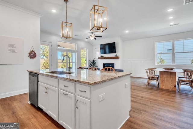 kitchen with white cabinets, a kitchen island with sink, light hardwood / wood-style flooring, pendant lighting, and sink