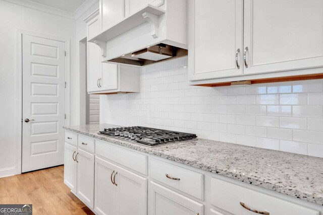 kitchen with white cabinetry, light hardwood / wood-style floors, custom exhaust hood, stainless steel gas stovetop, and decorative backsplash