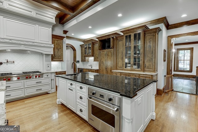 kitchen featuring white cabinetry, a center island with sink, light hardwood / wood-style flooring, stainless steel appliances, and decorative backsplash