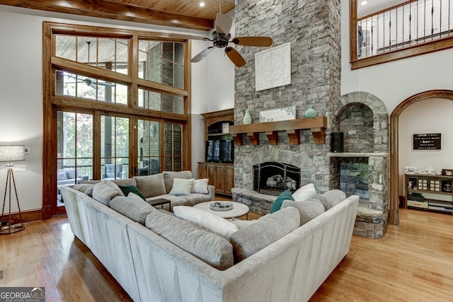 living room featuring hardwood / wood-style flooring, a towering ceiling, a stone fireplace, wooden ceiling, and beamed ceiling