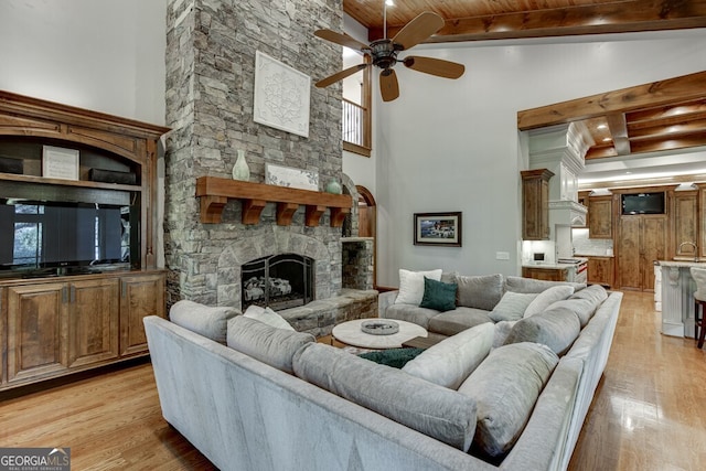 living room featuring a stone fireplace, a towering ceiling, light hardwood / wood-style floors, wooden ceiling, and beam ceiling