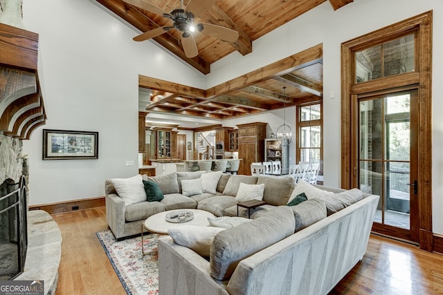 living room with a stone fireplace, vaulted ceiling with beams, wood ceiling, light wood-type flooring, and ceiling fan with notable chandelier