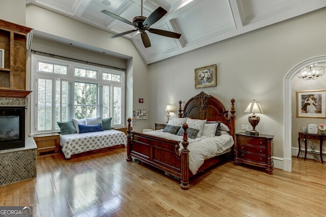 bedroom with coffered ceiling, ceiling fan with notable chandelier, and light hardwood / wood-style flooring