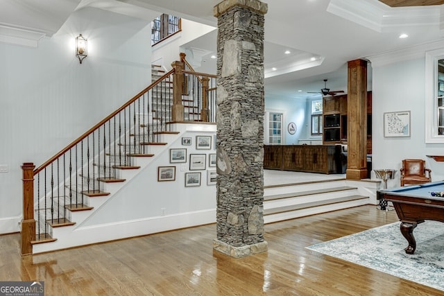 stairs with wood-type flooring, ornamental molding, decorative columns, and a raised ceiling