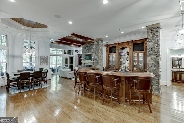 bar featuring ornate columns, a stone fireplace, pendant lighting, ornamental molding, and light wood-type flooring