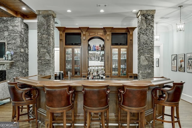 bar with decorative columns, crown molding, a fireplace, and light wood-type flooring