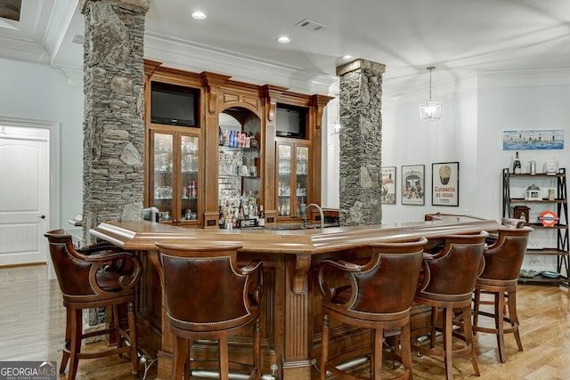 bar featuring ornamental molding, decorative columns, and light hardwood / wood-style flooring