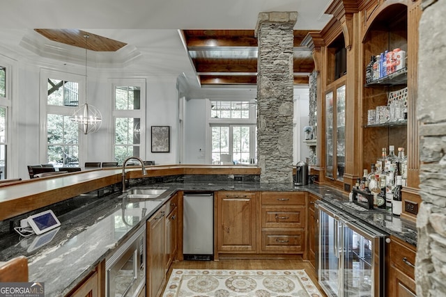 bar with sink, hanging light fixtures, stainless steel microwave, beverage cooler, and dark stone counters