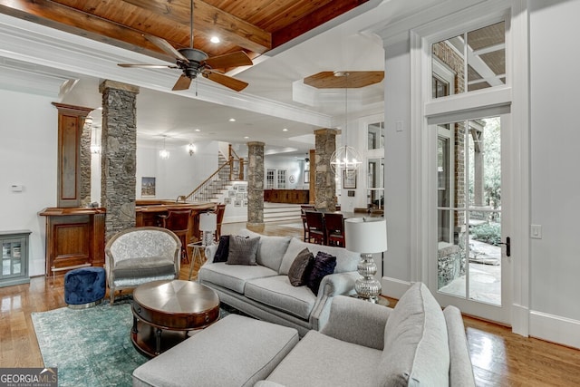 living room with ornate columns, ceiling fan with notable chandelier, wood ceiling, beam ceiling, and light hardwood / wood-style flooring