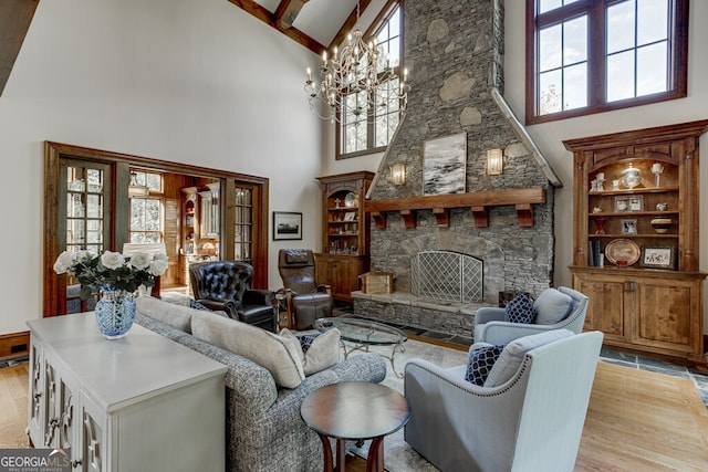 living room featuring beam ceiling, an inviting chandelier, light wood-type flooring, a towering ceiling, and a fireplace