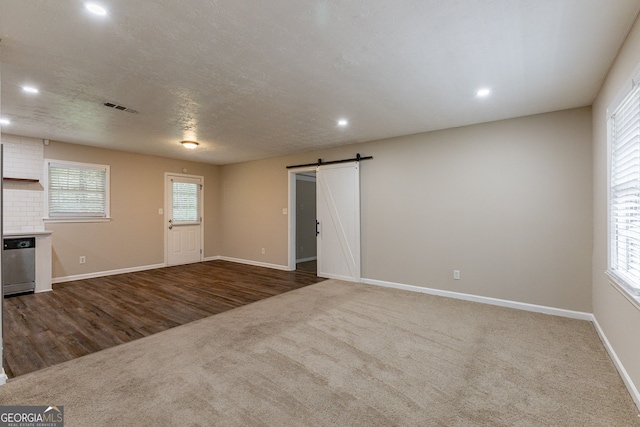 empty room with a textured ceiling, a barn door, and dark wood-type flooring