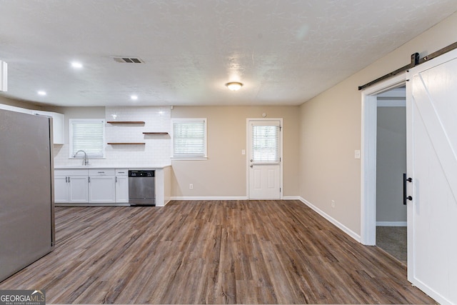 kitchen featuring tasteful backsplash, dark hardwood / wood-style flooring, white cabinetry, a barn door, and stainless steel appliances