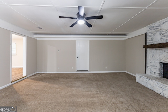 unfurnished living room featuring a stone fireplace, carpet floors, and ceiling fan