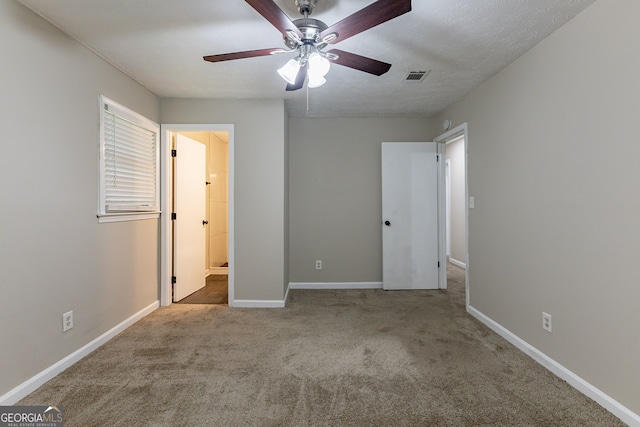 unfurnished bedroom featuring a textured ceiling, ensuite bath, light colored carpet, and ceiling fan