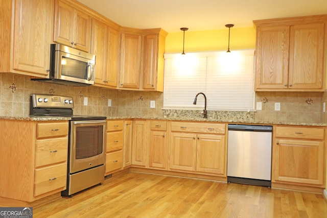 kitchen with light stone counters, light hardwood / wood-style flooring, sink, pendant lighting, and stainless steel appliances