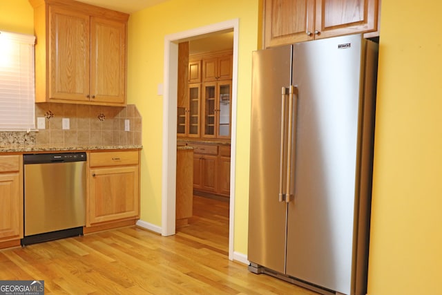 kitchen featuring light stone counters, stainless steel appliances, decorative backsplash, and light wood-type flooring