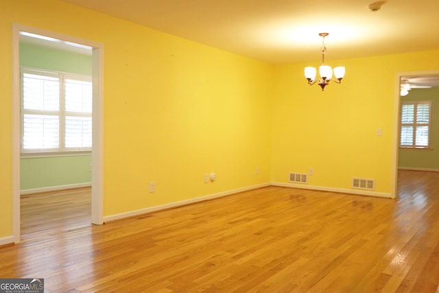 empty room with hardwood / wood-style floors and ceiling fan with notable chandelier