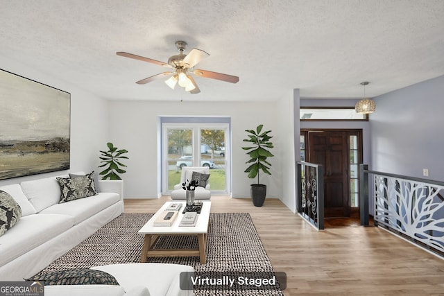 living room featuring ceiling fan, light wood-type flooring, and a textured ceiling