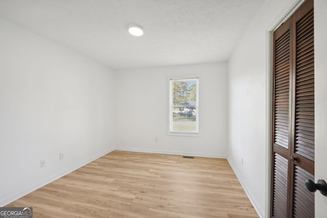 unfurnished bedroom featuring a textured ceiling, light wood finished floors, a closet, and baseboards