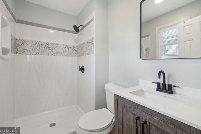 bathroom with tiled shower, vanity, and toilet