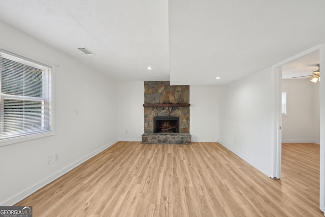 unfurnished living room with a stone fireplace, plenty of natural light, and light hardwood / wood-style floors