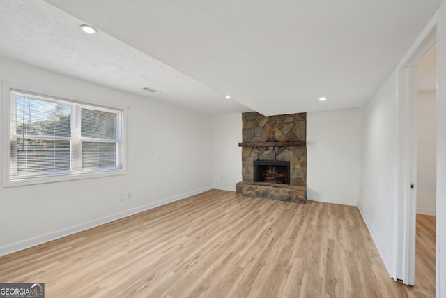 unfurnished living room with a stone fireplace, light wood-style flooring, and baseboards