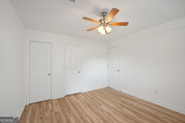 unfurnished bedroom with two closets, light hardwood / wood-style floors, and ceiling fan