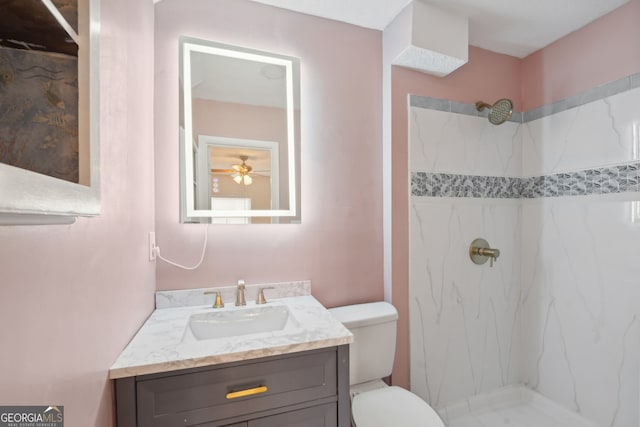 bathroom with vanity, ceiling fan, toilet, and a tile shower