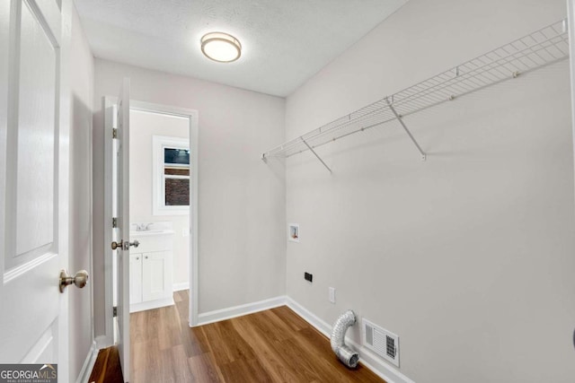 clothes washing area with hookup for an electric dryer, hookup for a washing machine, a textured ceiling, and hardwood / wood-style flooring