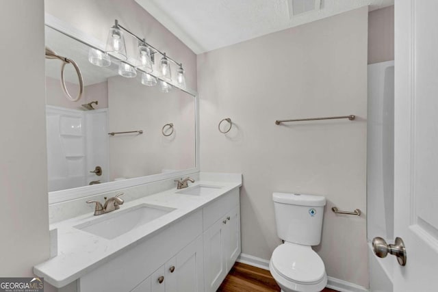 bathroom featuring toilet, wood-type flooring, vanity, a textured ceiling, and walk in shower