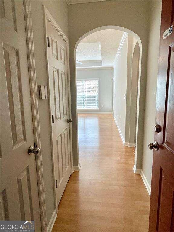 hall with light hardwood / wood-style floors, crown molding, and a textured ceiling