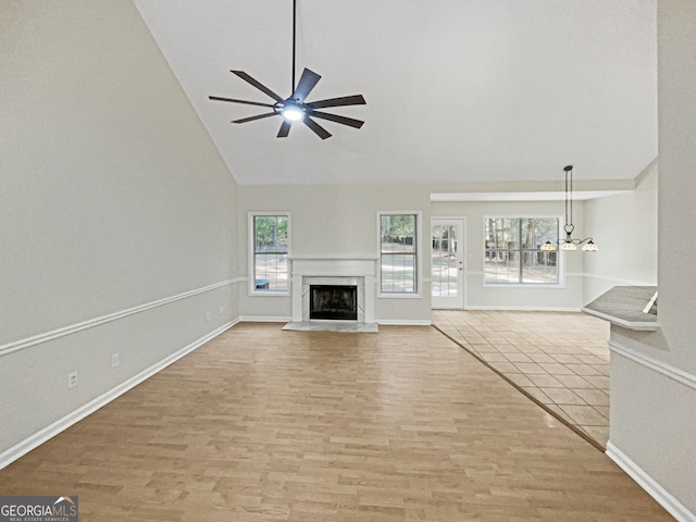 unfurnished living room with a premium fireplace, high vaulted ceiling, ceiling fan with notable chandelier, and light wood-type flooring