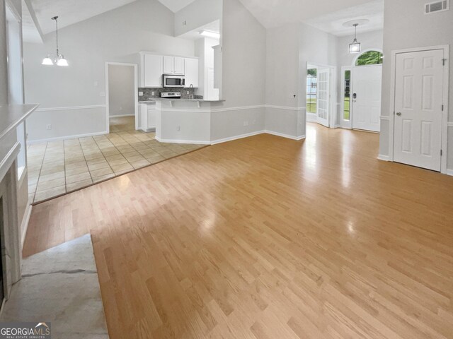 unfurnished living room with a premium fireplace, high vaulted ceiling, ceiling fan with notable chandelier, and light wood-type flooring