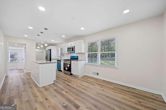 kitchen featuring a kitchen island, hanging light fixtures, white cabinetry, stainless steel appliances, and light hardwood / wood-style flooring