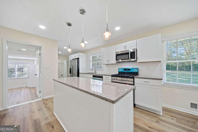 kitchen featuring appliances with stainless steel finishes, hanging light fixtures, white cabinets, and light hardwood / wood-style floors