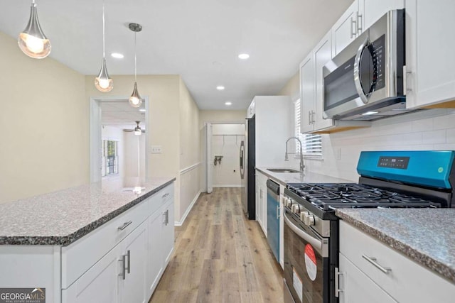 kitchen with decorative backsplash, appliances with stainless steel finishes, white cabinetry, light hardwood / wood-style floors, and decorative light fixtures