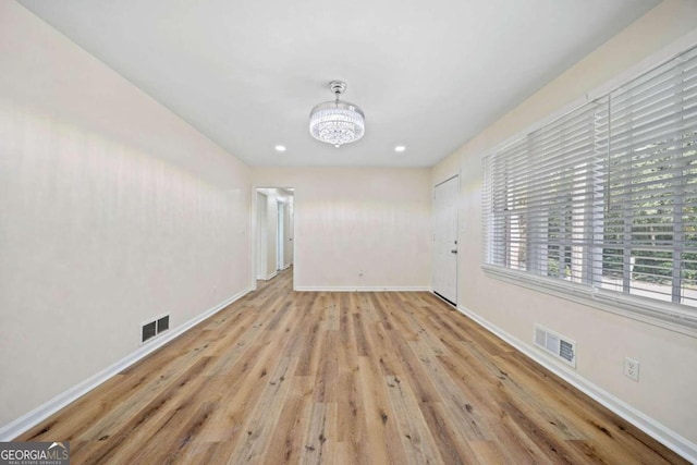 empty room featuring a chandelier and light wood-type flooring