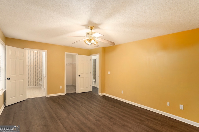 unfurnished bedroom featuring a walk in closet, ceiling fan, a textured ceiling, and dark hardwood / wood-style flooring